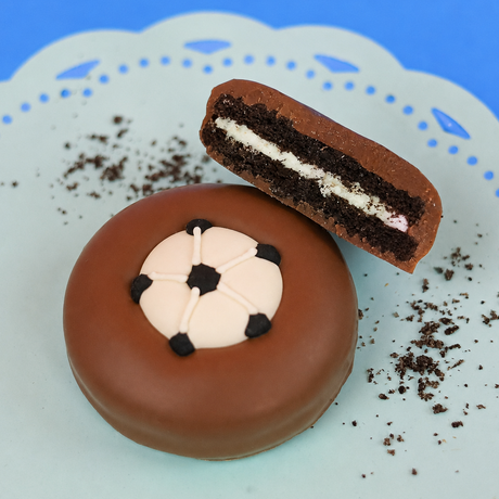 Milk chocolate soccer ball Oreo showing dark chocolate cookie layers and white cream filling on a mint green plate with blue background, handcrafted sports themed chocolate gift by Nibbles and Bits Scranton PA.