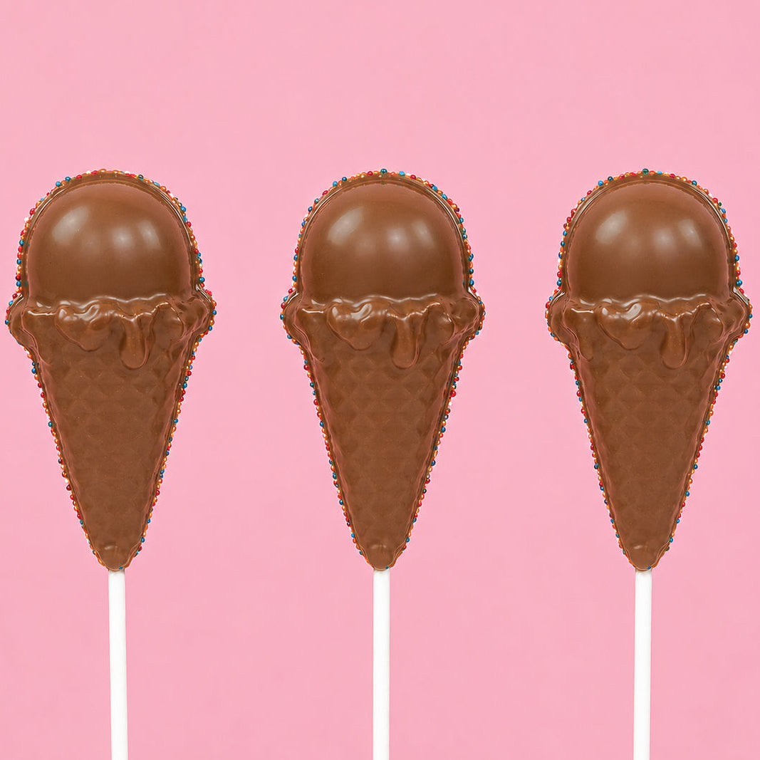 Three solid milk chocolate ice cream cone pops showing detailed molded waffle cone and rounded scoop with patriotic nonpareil border on white sticks against a pink background, handmade summer treat by Nibbles and Bits Scranton PA.