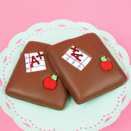 Two milk chocolate double dipped graham crackers on a mint green decorative plate, each hand-decorated with a red fondant apple and A+ notebook paper detail, teacher appreciation gift by Nibbles & Bits.