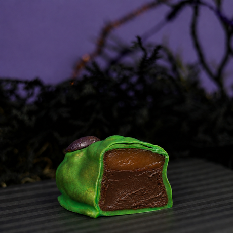 Witch Finger cut in half showing layers of fudgy brownie and golden caramel inside a green and milk chocolate shell.